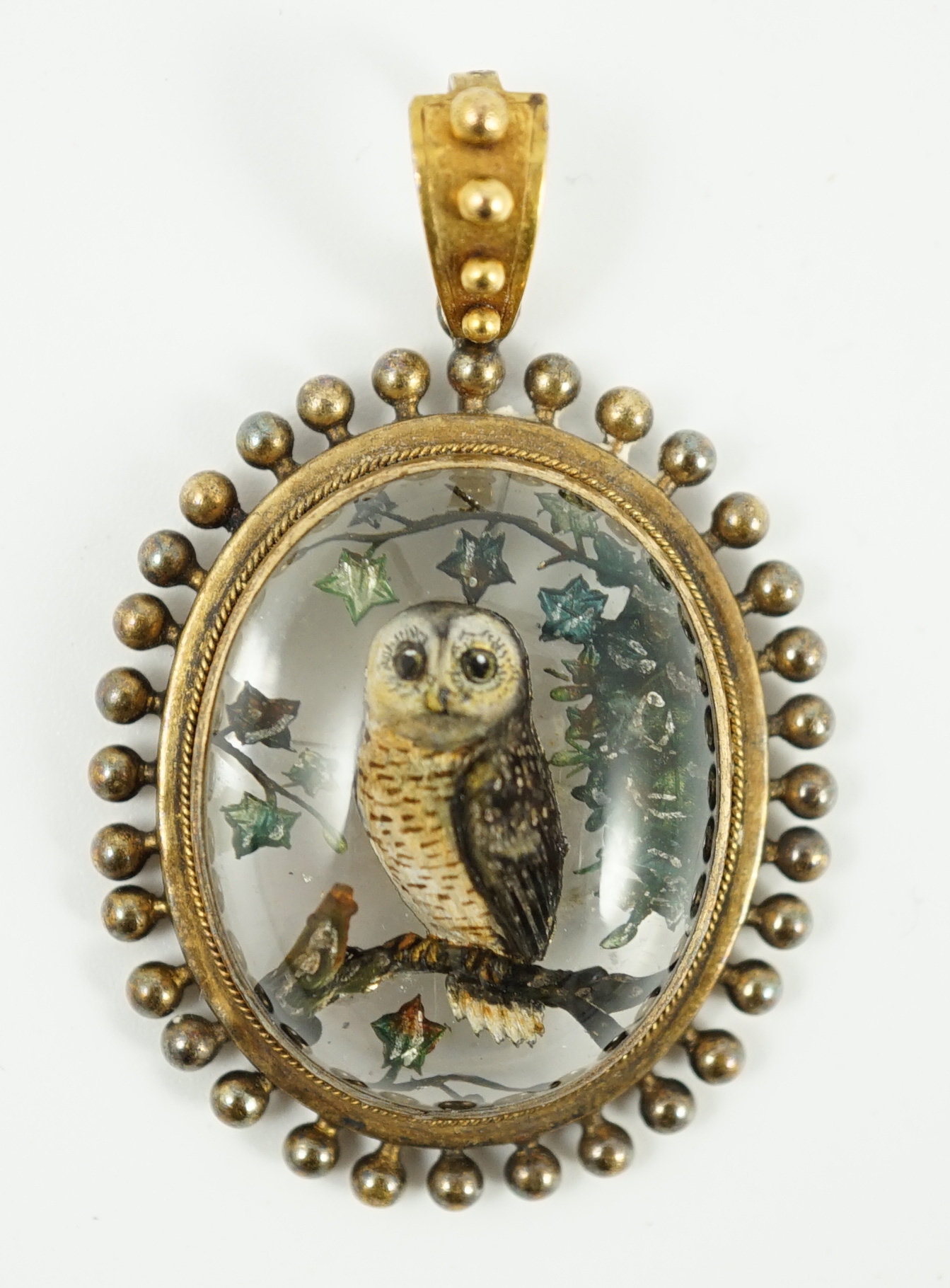 A Victorian yellow metal mounted Essex crystal oval pendant, depicting an owl upon a branch, amid foliage